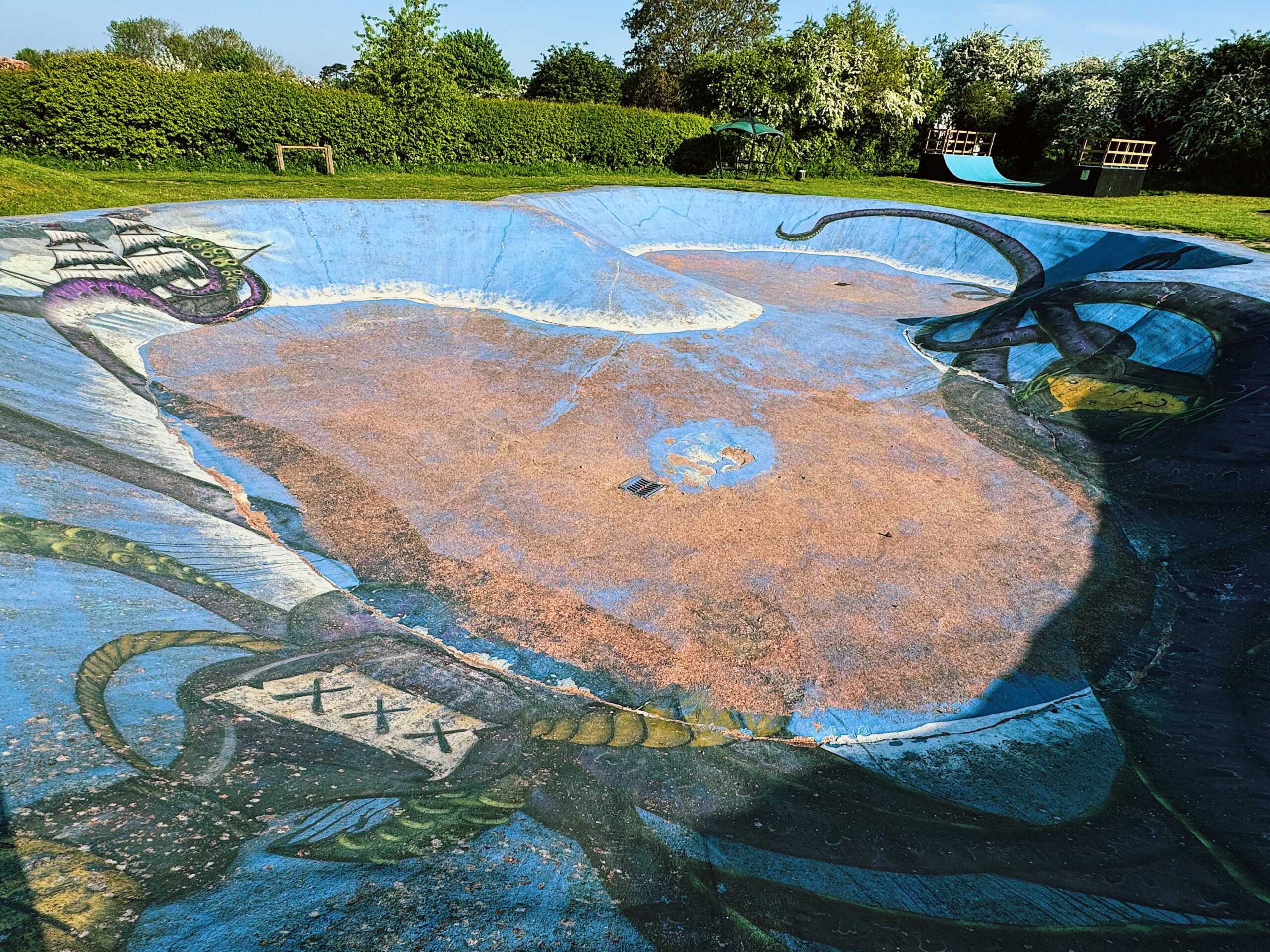 IMG_4035_VSCO image of a large blue skate bowl with octopus graffiti and skate ramp in the background